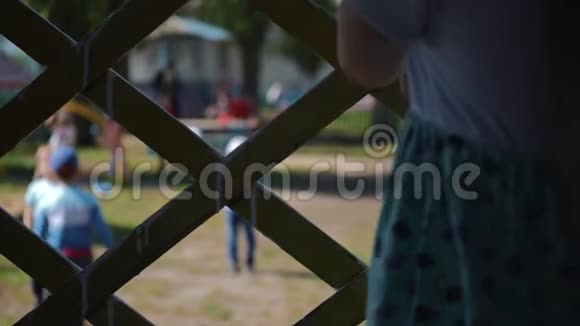 一个孤独的孩子拿着篱笆看着孩子们玩耍宏观的手视频的预览图