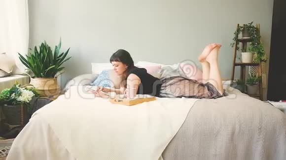 一个女人用平板电脑和喝咖啡躺在床上的肖像视频的预览图