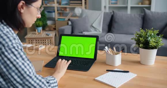 年轻女性在家里的餐桌上使用带有绿色模拟屏幕的笔记本电脑视频的预览图