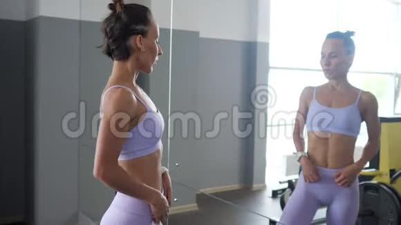 在健身房锻炼后女人正在看镜子上她运动的美丽身体视频的预览图