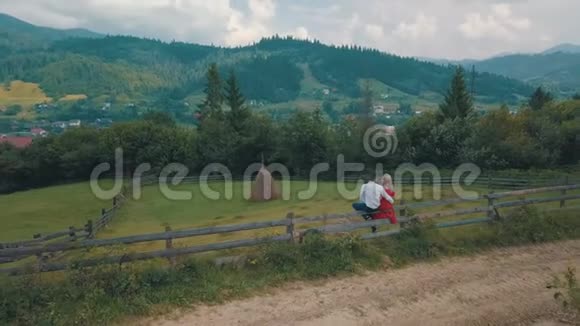 年轻夫妇一起坐在山边的篱笆上夏季多云天气从空中射击视频的预览图