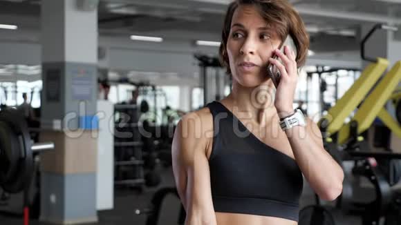 成熟的女人正在健身房和打电话的时候用哑铃做二头肌运动视频的预览图