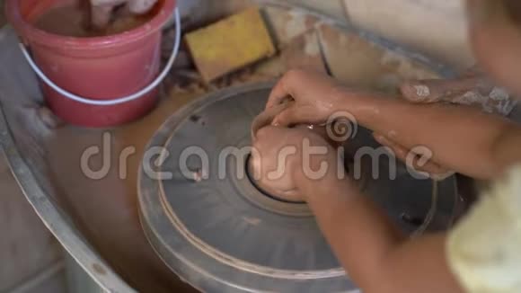 一个教师陶工教他的徒弟如何在陶工的轮子上做一个泥碗的慢速特写镜头视频的预览图