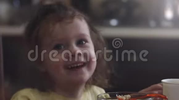 快乐的小女孩吃着粥和一杯牛奶作为早餐坐在桌子旁视频的预览图