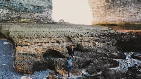 快乐的游客男子帮助妇女登上大低潮海岸珊瑚岩下巨大的自然拱门在埃特雷塔诺曼迪视频的预览图