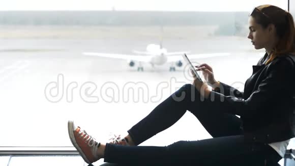 手里拿着现代平板电脑的女人坐在机场码头上视频的预览图