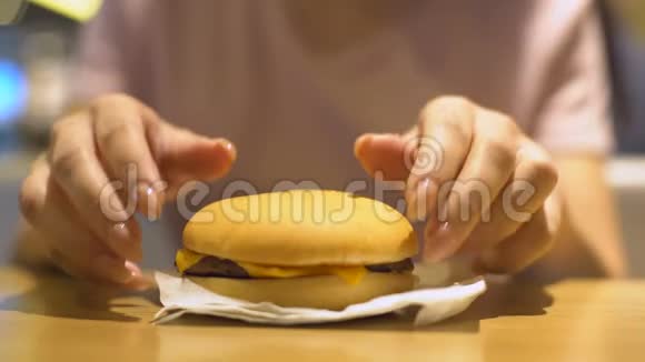 女人从桌子上拿美味的芝士汉堡不健康的饭菜肥胖的风险视频的预览图