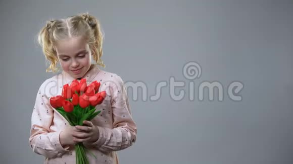 可爱的女孩闻着鲜花在灰色的背景下微笑节日的心情视频的预览图