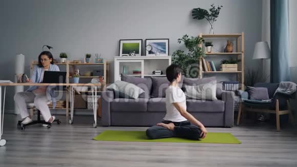 年轻的女士在家里做运动瑜伽的时候还在用电脑工作视频的预览图