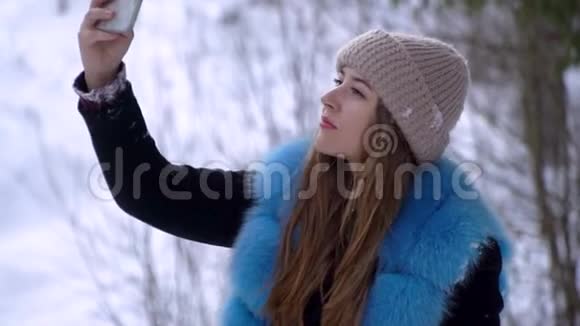 年轻漂亮的女孩走在白雪皑皑的冬林里她高兴一个女孩正在智能手机上拍照做一个视频的预览图