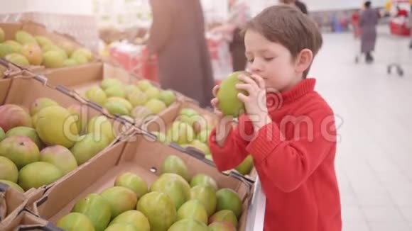有趣的小男孩在超市的家庭购物中从盒子里摘芒果视频的预览图