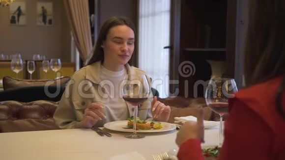两个女孩坐在餐厅里一边聊着天一边笑着吃着美味的菜肴一边在舒适的午餐中喝着酒视频的预览图