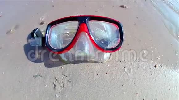 一个潜水面具躺在沙质的海岸上海浪在阳光明媚的日子里在上面冲浪慢速运动标准运动视频的预览图