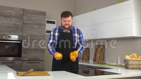 奥卡西安男厨师穿着围裙在现代厨房里摆弄橘子慢动作视频的预览图