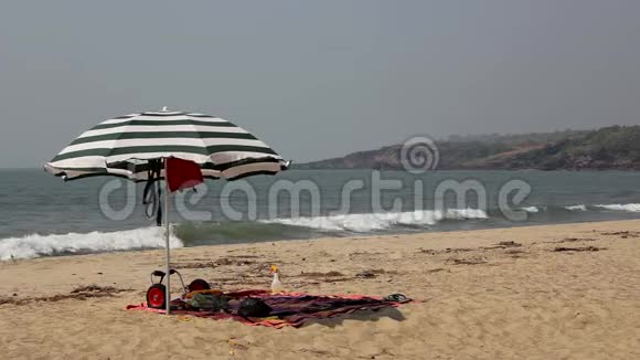 大条纹太阳伞在沙滩上迎着大海在晴朗的蓝天下掀起海浪视频的预览图