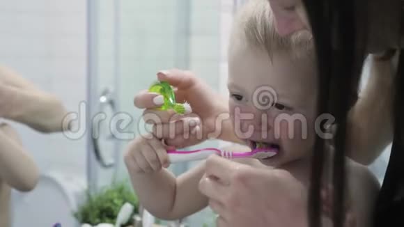 妈妈教孩子刷牙妈妈和孩子在刷牙时看镜子卫生概念视频的预览图