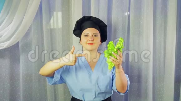 一个穿着围裙做饭的女人微笑着手里拿着一份绿色沙拉把她的手放在上面视频的预览图