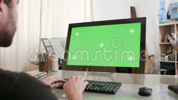 年轻的艺术家在电脑前工作显示器上有绿色的屏幕视频的预览图