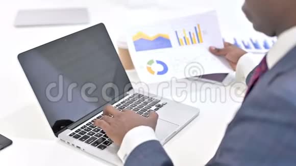 非洲商人在笔记本电脑和阅读文件的后视图视频的预览图