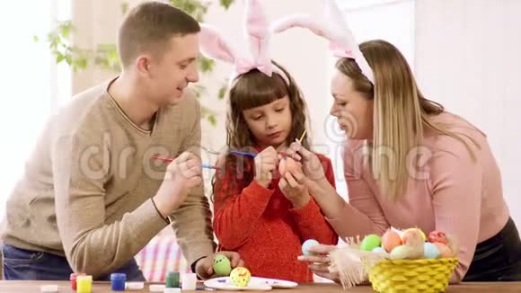 妈妈和女儿在兔子耳朵和爸爸装饰鸡蛋复活节假期视频的预览图