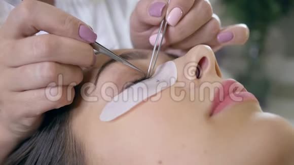 睫毛延伸专业师傅用钳子把人工睫毛贴在女人的眼睛上视频的预览图