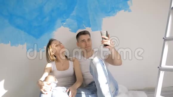 幸福的一对情侣坐在梯子附近的地板上一边拍照一边修理视频的预览图
