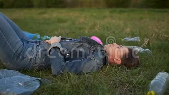 悲伤的女人躺在草地上的塑料垃圾中用手捂住他的脸环境消耗视频的预览图