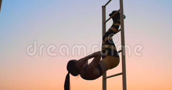 一幅强壮的年轻女子双腿向上挂在墙上的画像健身妇女表演吊腿动作视频的预览图
