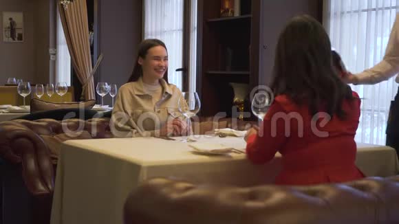 服务员在餐厅里的女孩的杯子里倒酒两个积极的女朋友坐在舒适的视频的预览图