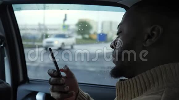 黑色男人浏览智能手机的肖像是在雨天在城市里骑汽车视频的预览图