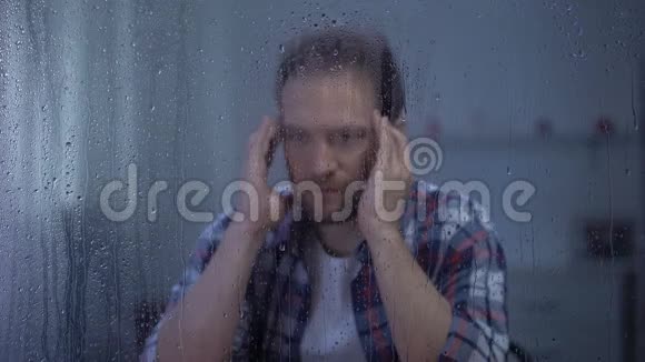 疲惫的中年男子在雨窗后按摩太阳穴偏头痛视频的预览图