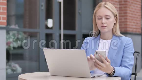 年轻的女商人使用智能手机和笔记本电脑坐在户外视频的预览图