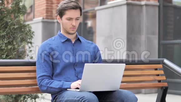 坐在户外的年轻人背疼手提电脑视频的预览图