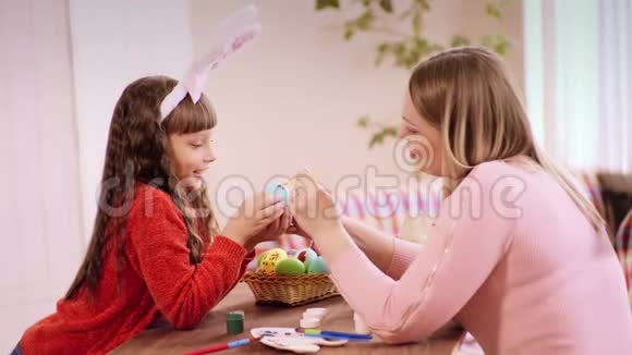 母亲和女儿一起在一张桌子上画复活节彩蛋在复活节之前玩得开心谈论事情视频的预览图