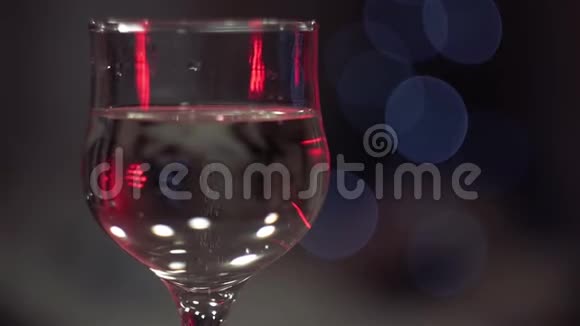 一杯有气泡的香槟被红光照亮站在眩光闪烁的灯光在背景中视频的预览图