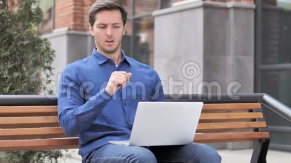 坐在户外的年轻人在笔记本电脑上工作时咳嗽视频的预览图