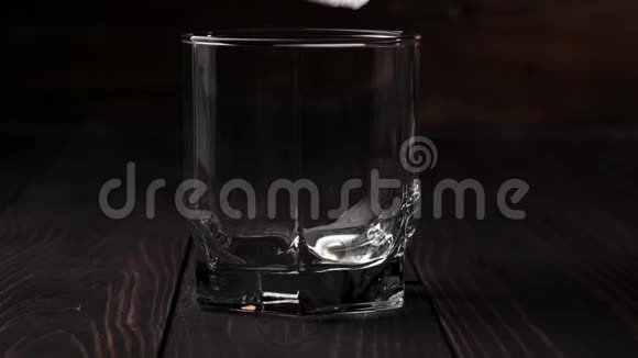 豪华威士忌冰块落在一杯威士忌中放在木制桌子上背景是木制的不倒翁威士忌视频的预览图