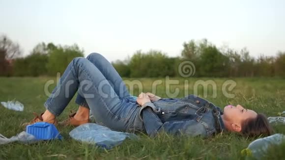 公园草地上一个穿着牛仔服的女孩躺在塑料垃圾堆中间照相机转来转去视频的预览图