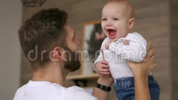 父亲和穿着白色t恤的小儿子玩看着他笑笑的宝贝看着镜头爱视频的预览图