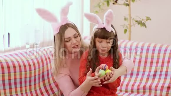 母女白种人的样子坐在沙发上的兔子耳朵里女孩们手里拿着复活节彩蛋视频的预览图