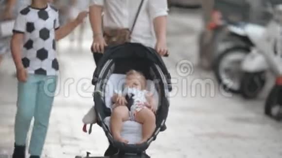 家人在城里散步妈妈带着婴儿车里的小女儿和大儿子视频的预览图