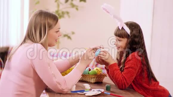 一个长着兔子耳朵的白人小女孩拿着鸡蛋她的母亲拿着刷子和视频的预览图