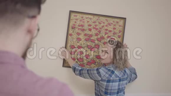 穿着衬衫的女人在背景中把漂亮的油画放在墙上前景中戴眼镜的胡子男视频的预览图