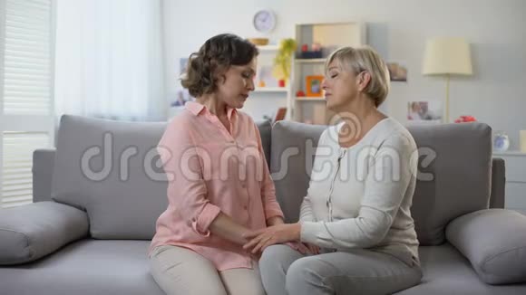 不快乐的成熟女性和女儿拥抱坐在家里的沙发上失去分手视频的预览图