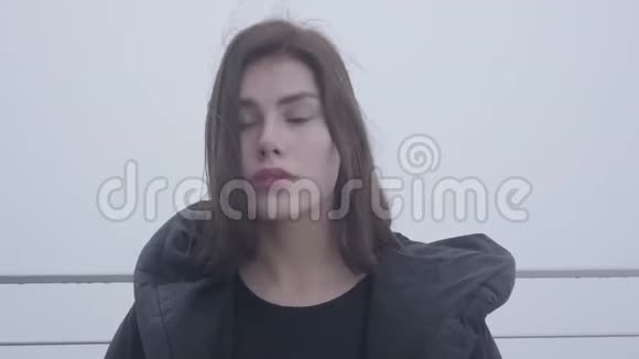 一个年轻可爱的女孩黑发站在黑色夹克衫在雾天户外的肖像视频的预览图