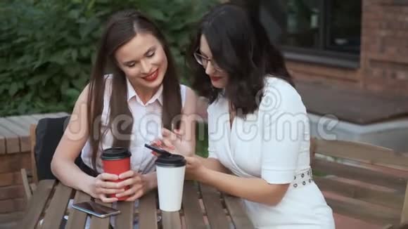 两个年轻女子坐在夏日咖啡馆的一张桌子旁愉快地聊天那女孩向她的朋友展示她身上的东西视频的预览图