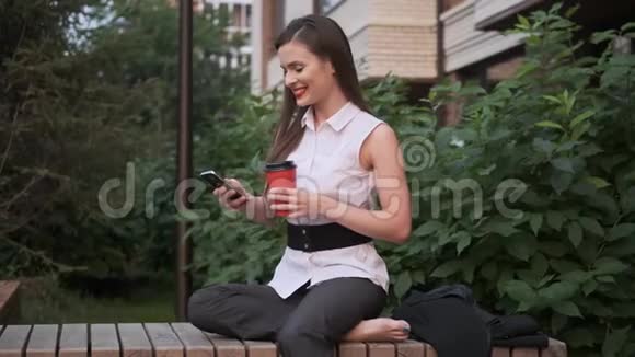 那年轻女子脱下鞋坐在长凳上休息女商人喝咖啡用视频的预览图