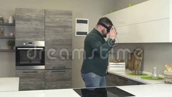 一个戴着蓝色虚拟现实眼镜的大胡子男人走过现代厨房新技术慢摩3d视频的预览图