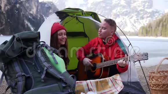 年轻夫妇坐在帐篷里在群山的背景下用吉他唱歌视频的预览图