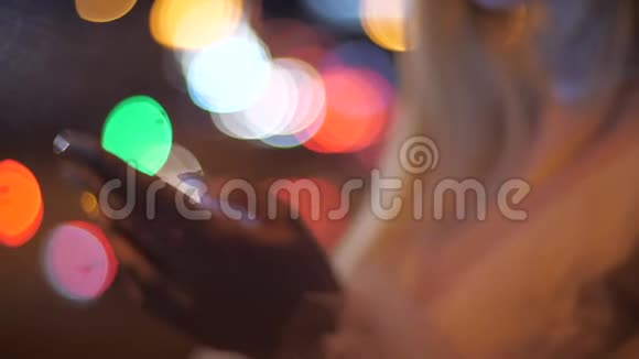 晚上在城市里用智能手机特写金发女人的手在城市街道的智能手机上输入信息视频的预览图